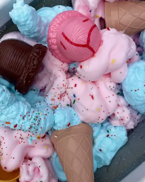Pink and blue shaving-cream foam with sprinkles and toy ice cream cones in a tray.